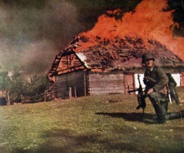 Unteroffizier vor einer brennenden Hütte