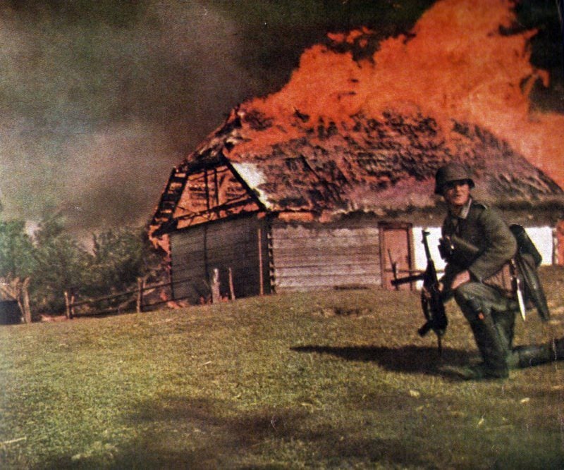 Unteroffizier vor einer brennenden Hütte