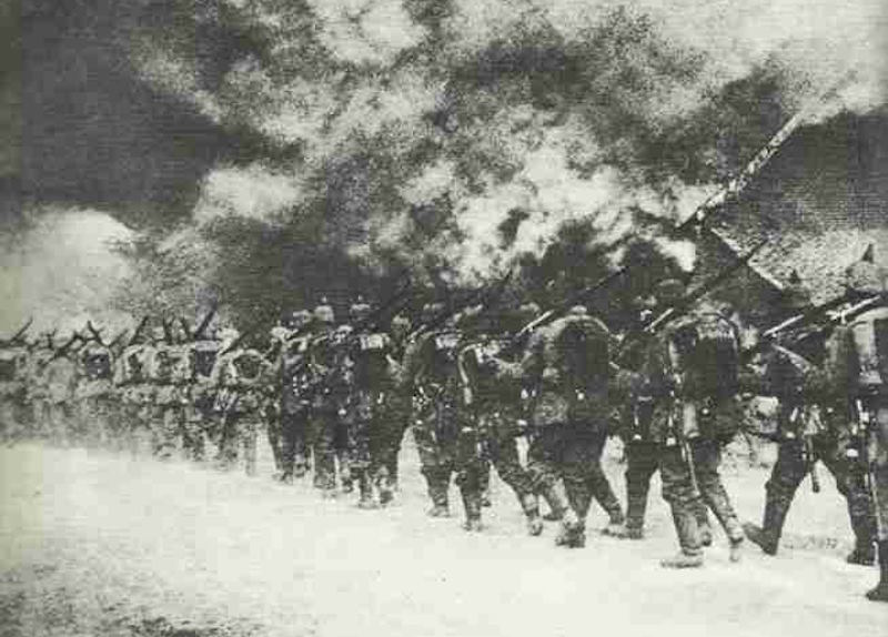 Deutsche Infanterie marschiert durch eine brennende französische Ortschaft